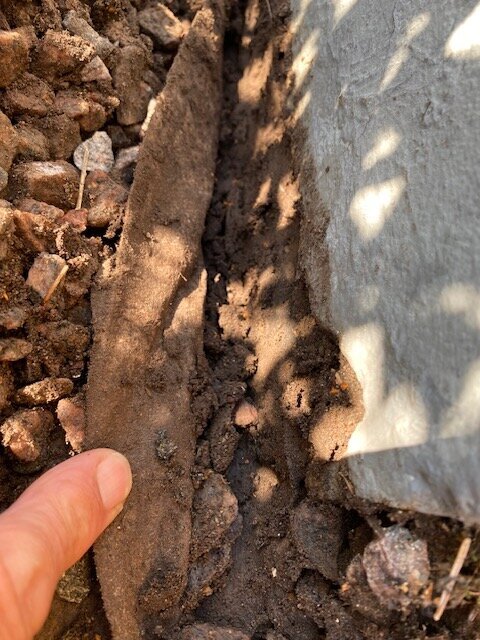 Grus och en presenning vid en husvägg; en hand visar ett rengjort område på en betongyta.