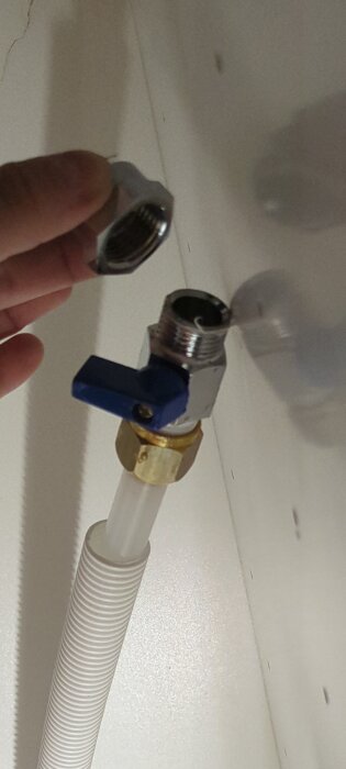 Hand håller en kopplingsdel ovanför en blå ballofixventil kopplad till en plastslang, demonstrerar en läckande installation.
