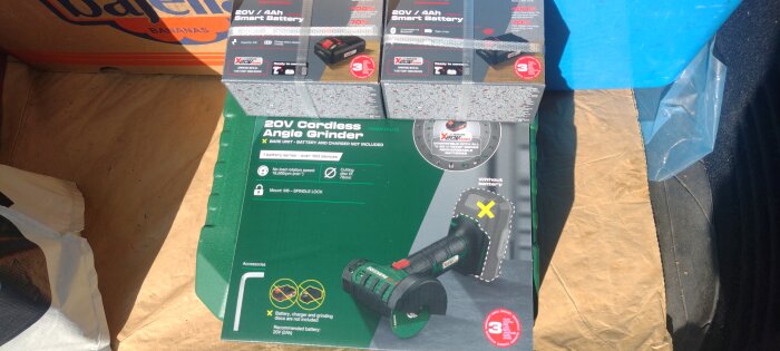 Förpackningar av två 20V/4Ah smarta batterier och en sladdlös vinkelslip på brun kartong i ett fordon.