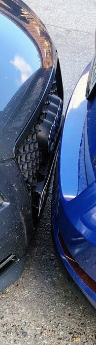 Närbild av två bilar parkerade mycket nära varandra, med fronterna nästan i kontakt.