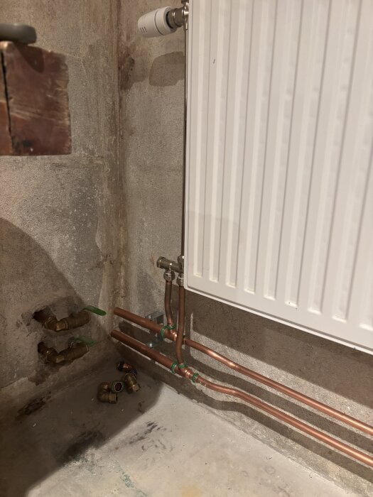 Rörledning till radiator i källaren, kopparrör, ventiler och kopplingar på betongvägg.