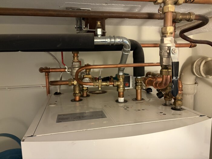 Värmesystem med rör och ventiler ovanpå en vit panna, relaterat till borttagning av element vid renovering.