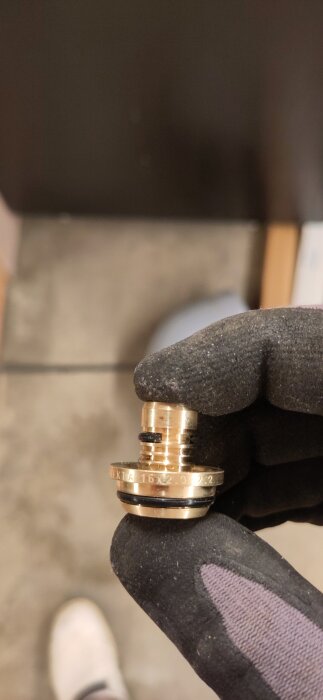 Anslutningsdel i mässing med text "Trio Perfekta 16x2,0-2,2" hålls i en handske, synlig svart o-ring.