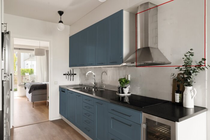 Modernt kök med blå skåp, svart bänkskiva och rostfri fläkt. Röd linje markerar utrymmet ovanför skåpen för möbelbräda.