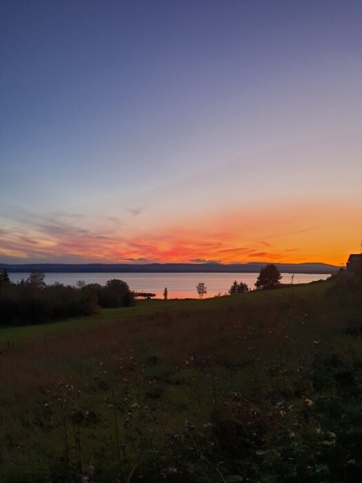 Solnedgång över sjö med färgglad himmel, omgiven av landskap och träd.