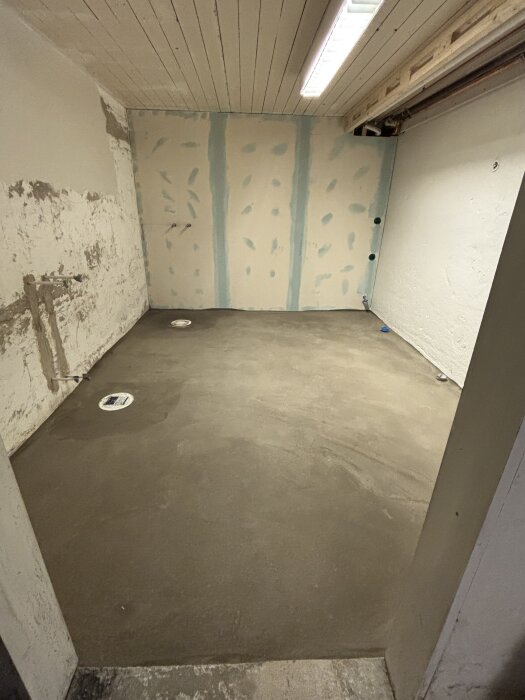 Nyflytspacklat badrumsgolv med korrekt fall mot dusch och badkarsbrunn, väggar under arbete.