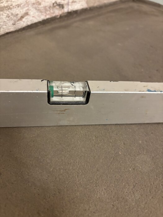 Bubbelvattenpass på nyslipat flytspackelgolv i badrum, visar korrekt lutning mot avlopp.