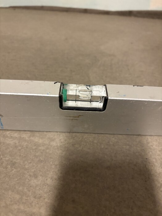 Vattenpass på flytspacklat golv i badrum, visar korrekt fall för avrinning mot dusch och badkarsbrunn.