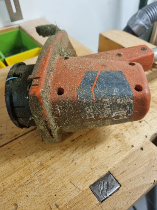 Gammal och sliten röd Husqvarna sladdmaskin med smutsig yta på träarbetsbänk.