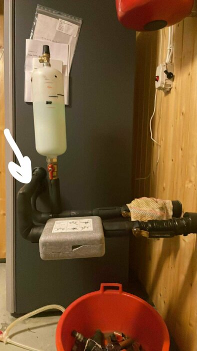 Montering av rör och ventil med anslutet vitt kärl; röret är pekat på och en röd hink med verktyg syns.