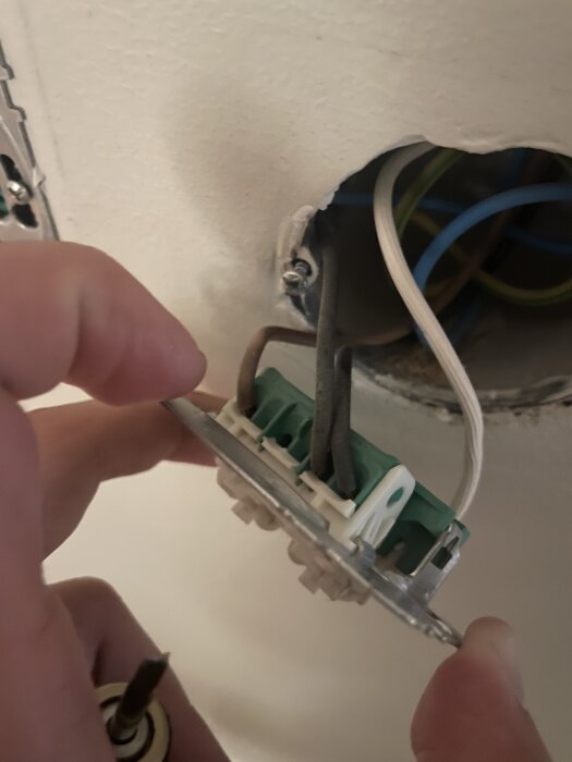 Hand håller en elkontakt med flera kablar, synlig elinstallation i tak.