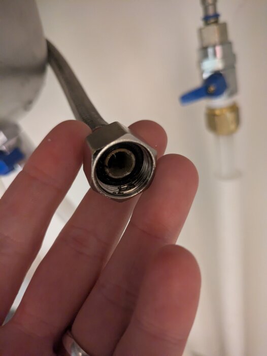 Närbild av en hand som håller en metallanslutning med en synlig gänga och en klämringsfitting i bakgrunden, del av en vatteninstallationsprocess.