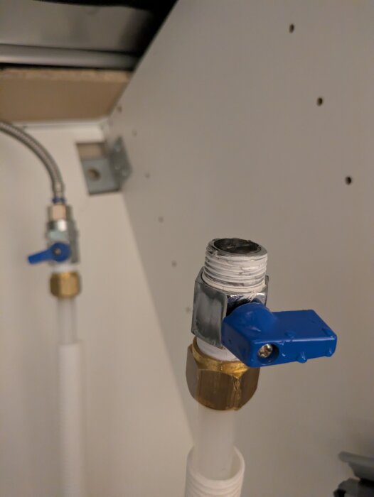Vitt rör med blå ventil och metallkoppling; en del av ett VVS-system.