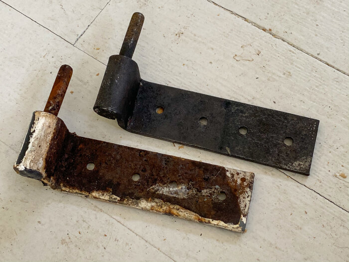 Två rostiga metallgångjärn på ett vitt underlag, med ett svart och ett mestadels reviderat för att testa bikarbonat för rengöring.