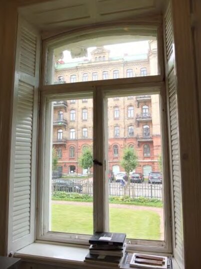 Fönster med innanförliggande fönsterluckor i gammal byggnad från 1880-talet i Göteborg, utsikt mot en tegelbyggnad.