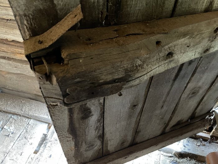 Gammalt trälås på en timrad bods dörr, med en handsmidd nyckel cirka 25 cm lång och en låskista i trä.