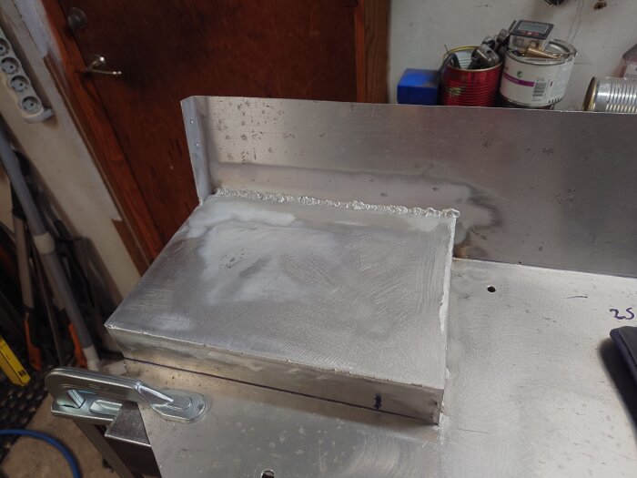 En aluminiumplåt har svetsats ihop och är fastklämd på en arbetsbänk i en verkstad.