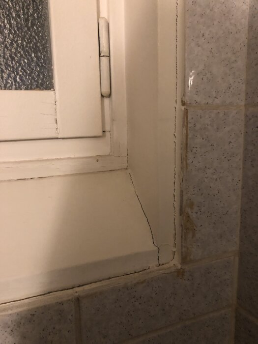 Sprucken färg och fog runt ett fönster i ett äldre duschutrymme med omgivande kakel på väggen.