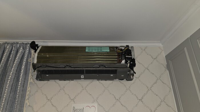 Luftvärmepump utan skydd, delvis isärplockad, monterad på vägg inomhus, med synliga komponenter och elanslutningar.