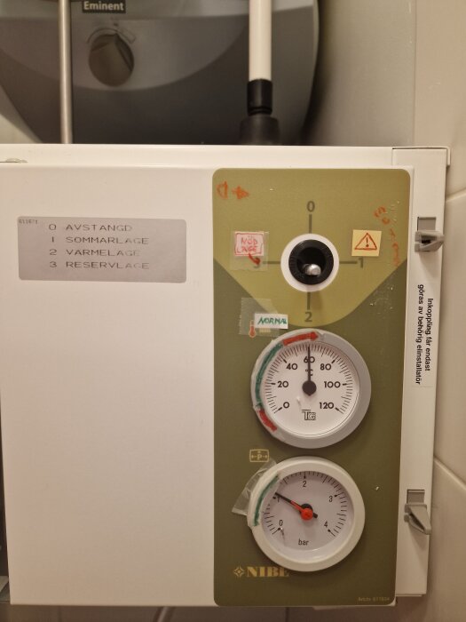 NIBE värmepanna modell EVC13 med tre lägen: avstängd, sommarläge, värmeläge, reservläge. Två mätare visar temperatur och tryck.