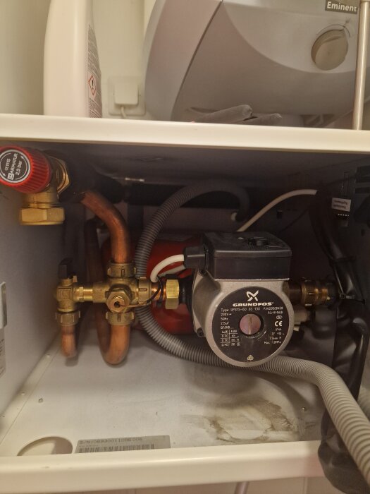 Cirkulationspump och rör i ett skåp bredvid en vattenvärmare, del av vattenburen golvvärmeanläggning i fritidshus på Gotland.