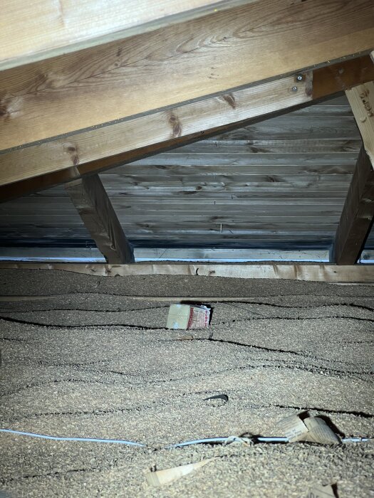 Vind med spån och träbjälkar synliga, kartong syns ovanpå spånlagret.