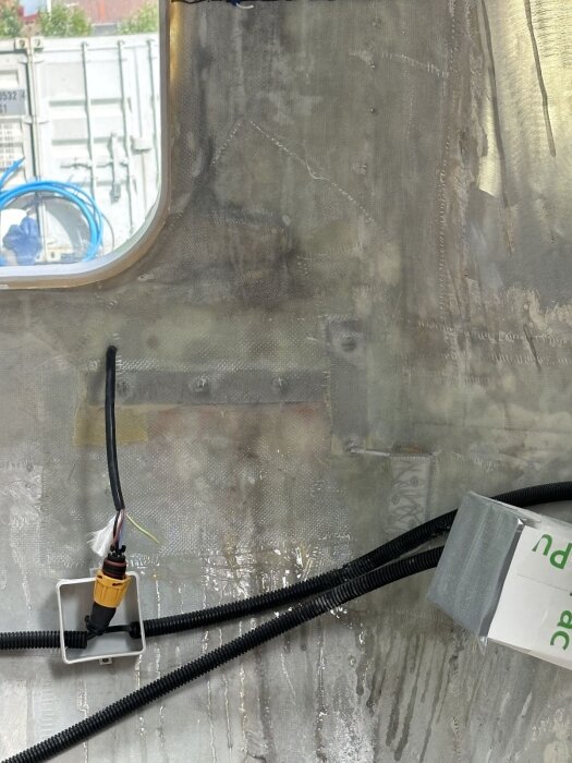 Aluminiumvinkelfäste limmat och täckt med glasfiber i en bastuvagn, med kablar och anslutningar nära ett litet fönster.