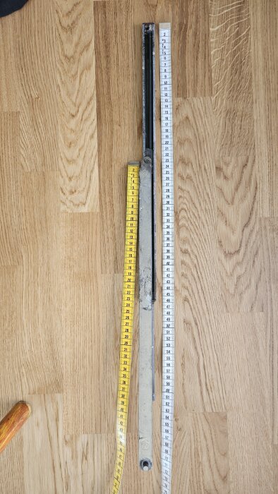 En dörrbroms av märket Fix ligger på trägolv, mätt med en vit och en gul måttstock.