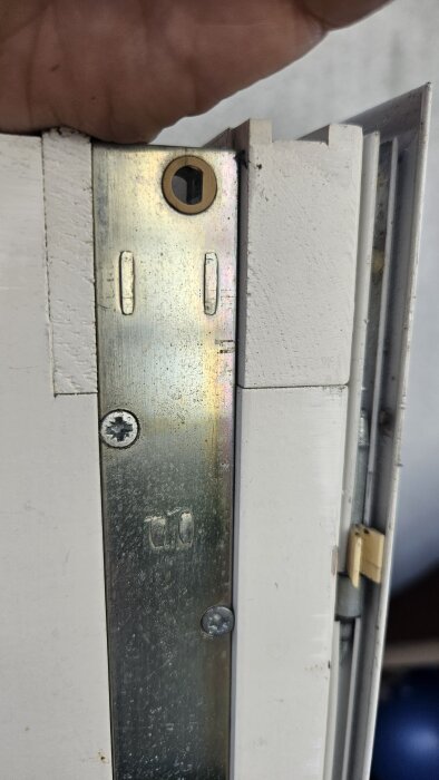 Närbild på en metallplatta på en dörrkarm med skruvar och ett ovalt, fasat hål för en spärrpinne, del av en dörrbroms.