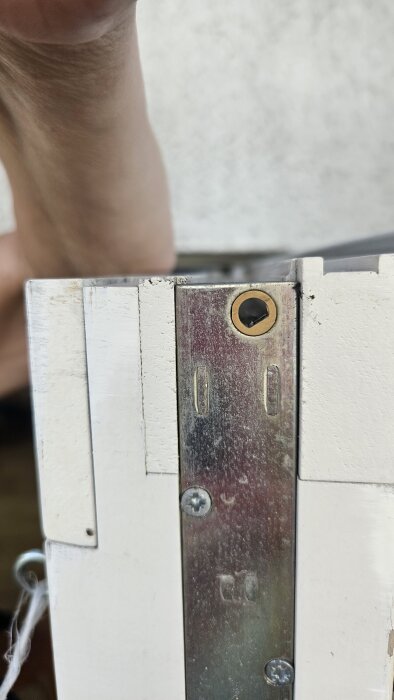 Närbild av en dörrkarm med en metallskena som har en roterande fasning för spärrpinnen, med två skruvar fästa i metallen.