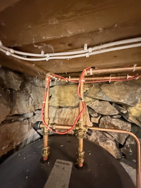 Röd värmekabel draget längs vattenrör i en källare med synliga stenväggar och trätak, visar både isolerade och oisolerade sektioner.