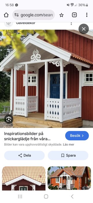 Röd stuga med snickarglädje på farstukvisten, vita detaljer och blå dörr. Huset har ett tegeltak och omges av grönska.