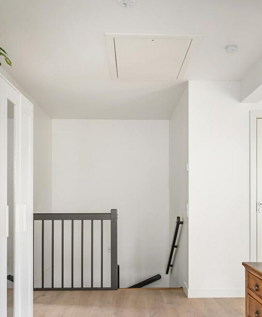 Vind med vitmålad vägg, trappräcke och taklucka, potentiellt användbar som förråd.