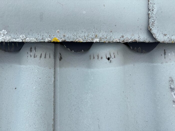 Närbild av takpannor med mossa och korrigeringar nära nocken, uppvisande ett installationsfel.