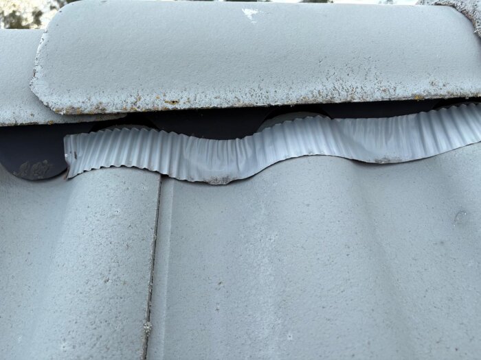 Takpannor närmast nock lagda för långt ner med synlig vågig tätning ovanpå, små skador och rostfläckar kan också ses.