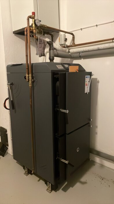 En modern vedeldad panna med kopparledningar och tryckmätare i ett tekniskt rum.