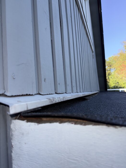 Alt-tex: Närbild av vit panelvägg med ett plåtbleck som är infällt ovanför altantak, med en öppning in till isolering.