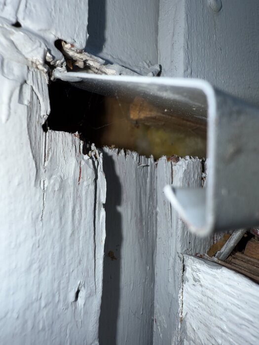 Öppet hål i träpanel där altantak är infäst, med synligt plåtbleck och tillgång till isoleringen bakom.