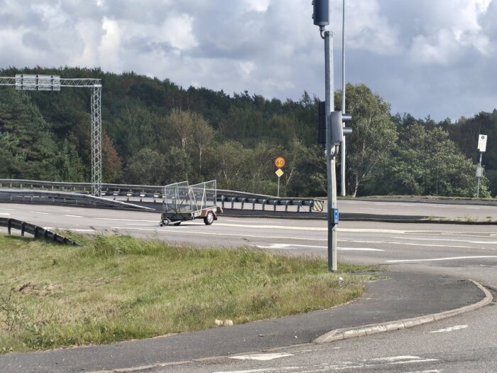 Släpvagn lastad med träram står på vägen vid en landsvägskorsning med skog i bakgrunden.