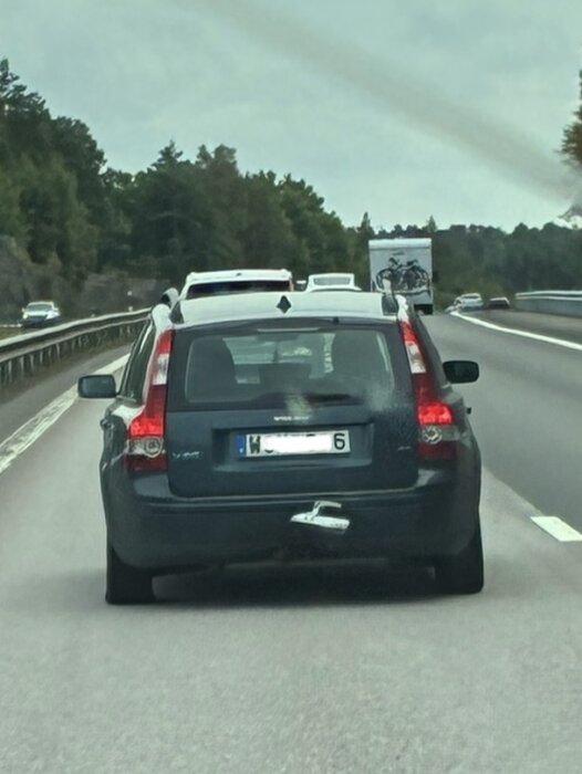 En bil med avtagbart dragkroksskydd som glidit ner på motorväg med omgivande skog och flera fordon i bakgrunden.