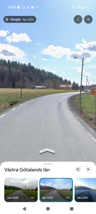 Landsväg i Västra Götaland med stolpar och en byggnad i bakgrunden, fotograferad i april 2023 under en klarblå himmel.