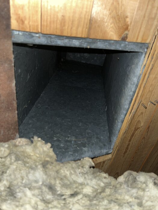 En närbild av en plåttakhuv som är installerad i taket, med isolering av stenull synlig i nederkanten av bilden.