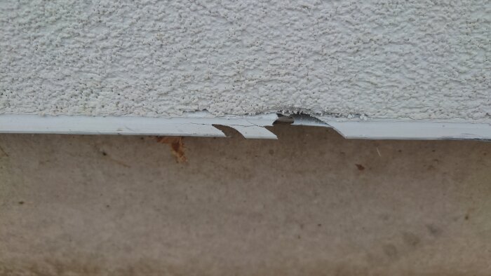 Skadad vit avvattningslist eller profil under en putsad vägg, cirka 15 cm lång skada.