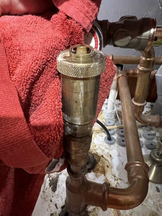 En röd trasa runt en metallventil ansluten till kopparrör. Ventilen liknar en säkerhetsventil, vatten läcker.