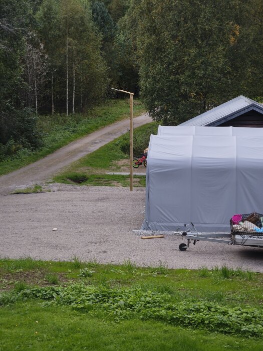 Gårdsplan med grusväg och stång som håller en LED-lampa, omgiven av skog och tältliknande struktur.