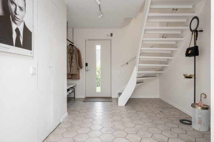 Vit målad trappa i ett modernt inrett rum med vitt kakelgolv och beige dörr i bakgrunden.