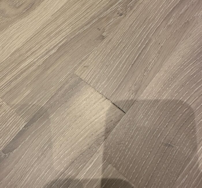 Närbild av parkettgolv med tydlig glipa mellan kortsidorna av två brädor, skugga syns på golvet.