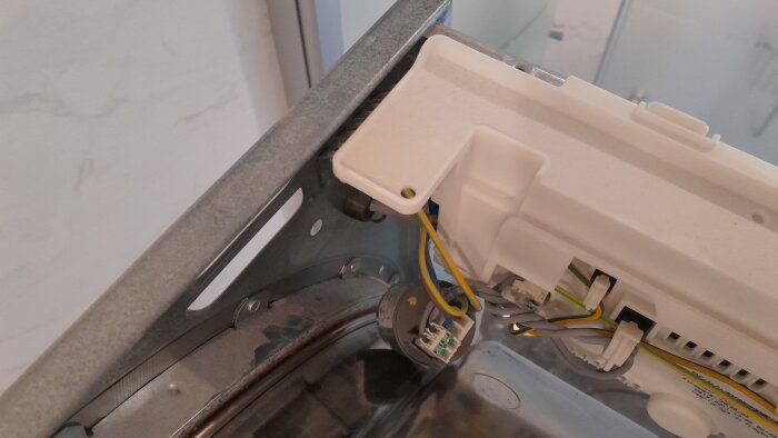 Öppnad maskin med synliga interna komponenter, inklusive en grå rund del och kablar som är anslutna till en vit plastdel.