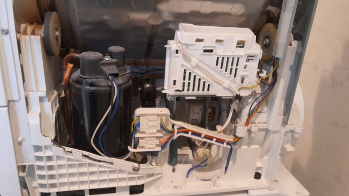 Öppen insida av en tvättmaskin med synliga kablar, ett styrkort och andra komponenter, omgivna av vit plast och metall.