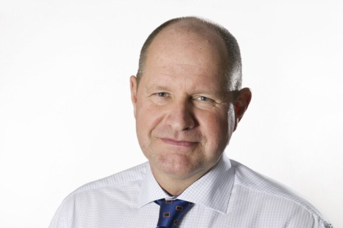 Okänd person i kostym och slips, mot vit bakgrund.